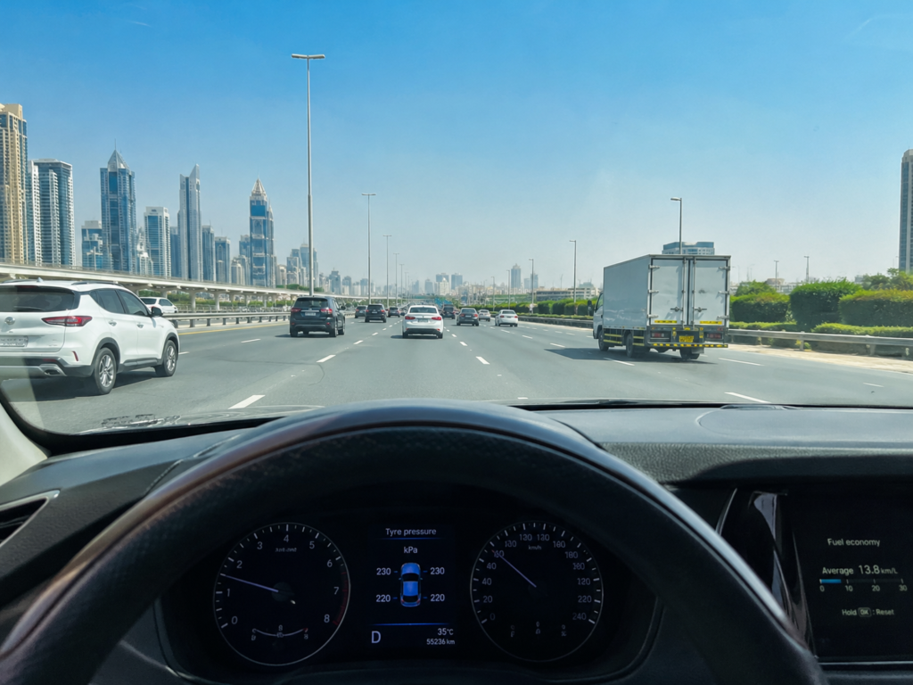 Driver's view of a UAE highway with dashboard fuel economy indicator visible, illustrating fuel-saving driving habits.